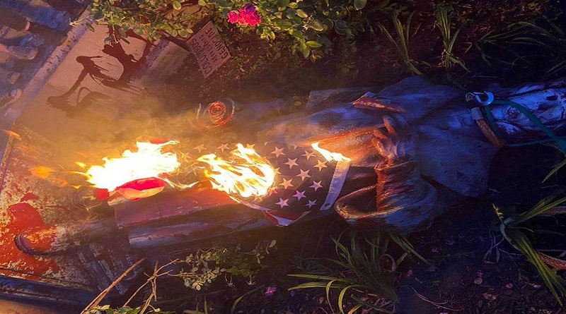 Manifestantes antirracistas derriban y prenden fuego una estatua de Cristóbal Colón junto a una bandera de EE.UU.